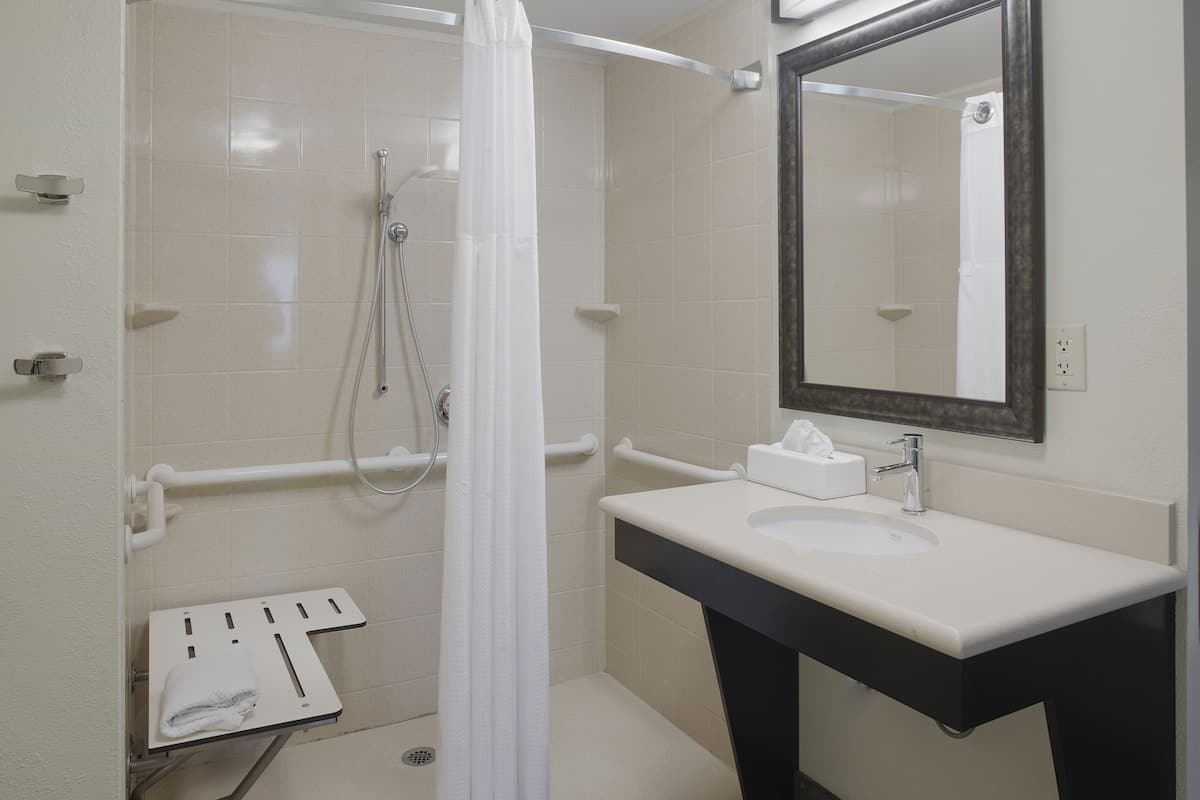 A bathroom with a white sink, a mirror, a shower with a curtain, and a towel rack.