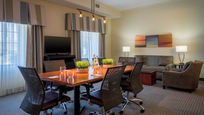 A hotel room with a dining area, a television, a sofa, and a lamp.