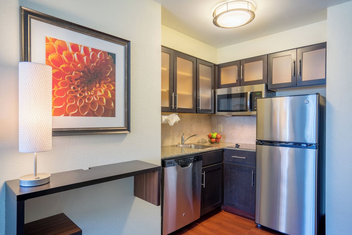A modern kitchen with stainless steel appliances, dark cabinetry, and a framed floral artwork on the wall.
