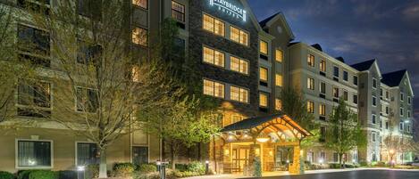 A multi-story hotel with a stone facade, a lit entrance, and a clear sky.