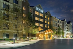 A multi-story hotel with a stone facade, a lit entrance, and a clear sky.