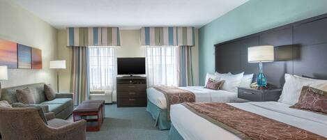 A hotel room with a sofa, two beds, a TV, a dresser, and a lamp.