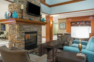 A lobby with a stone fireplace, comfortable seating, a flat-screen TV, and a bookshelf.