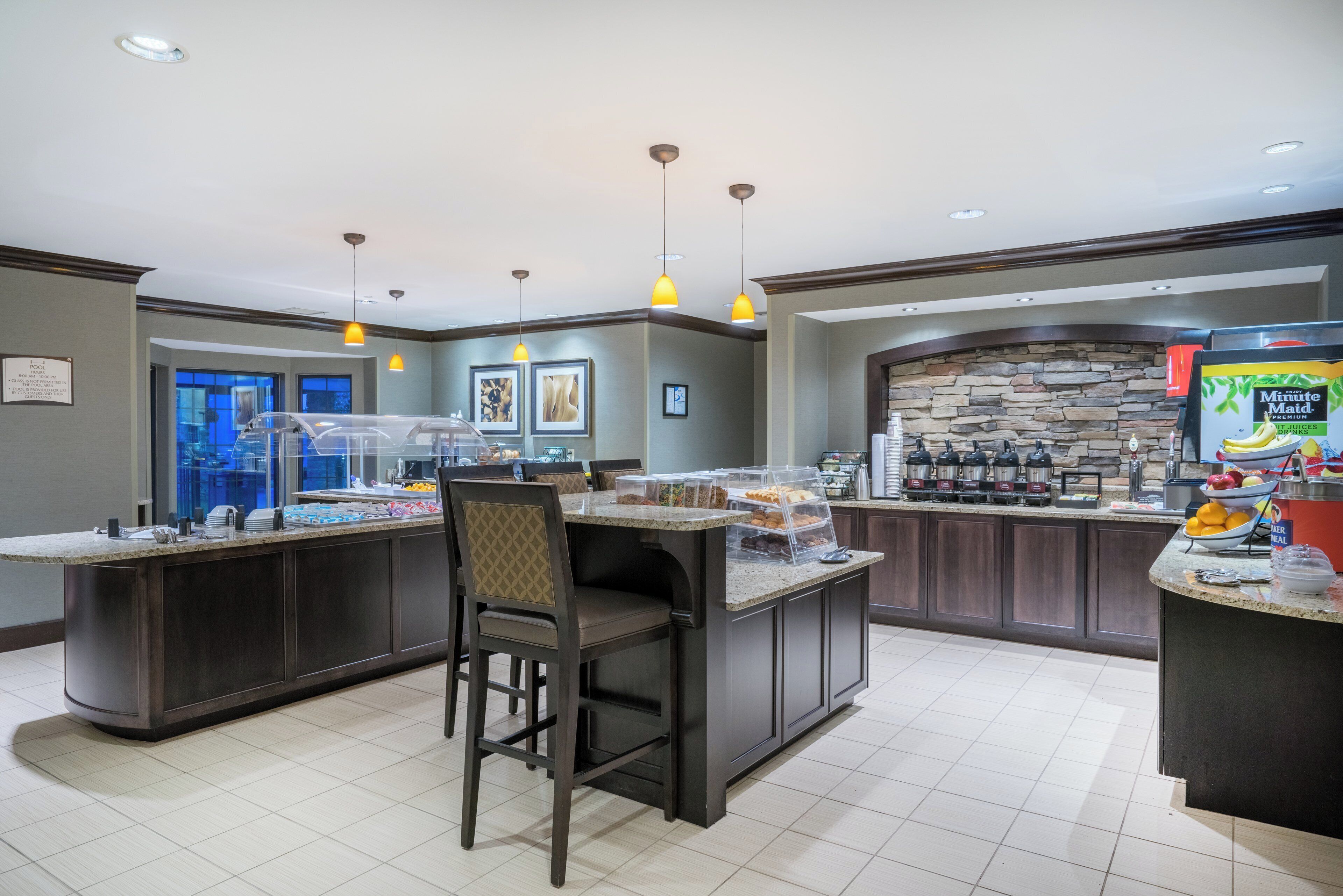 A hotel lobby with a self-service breakfast bar, seating area, and a stone accent wall.