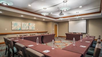 A conference room with a long table, chairs, a projector screen, and a carpeted floor.