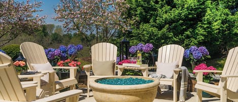 Un patio con sillas Adirondack, un recipiente decorativo grande y diversas flores.