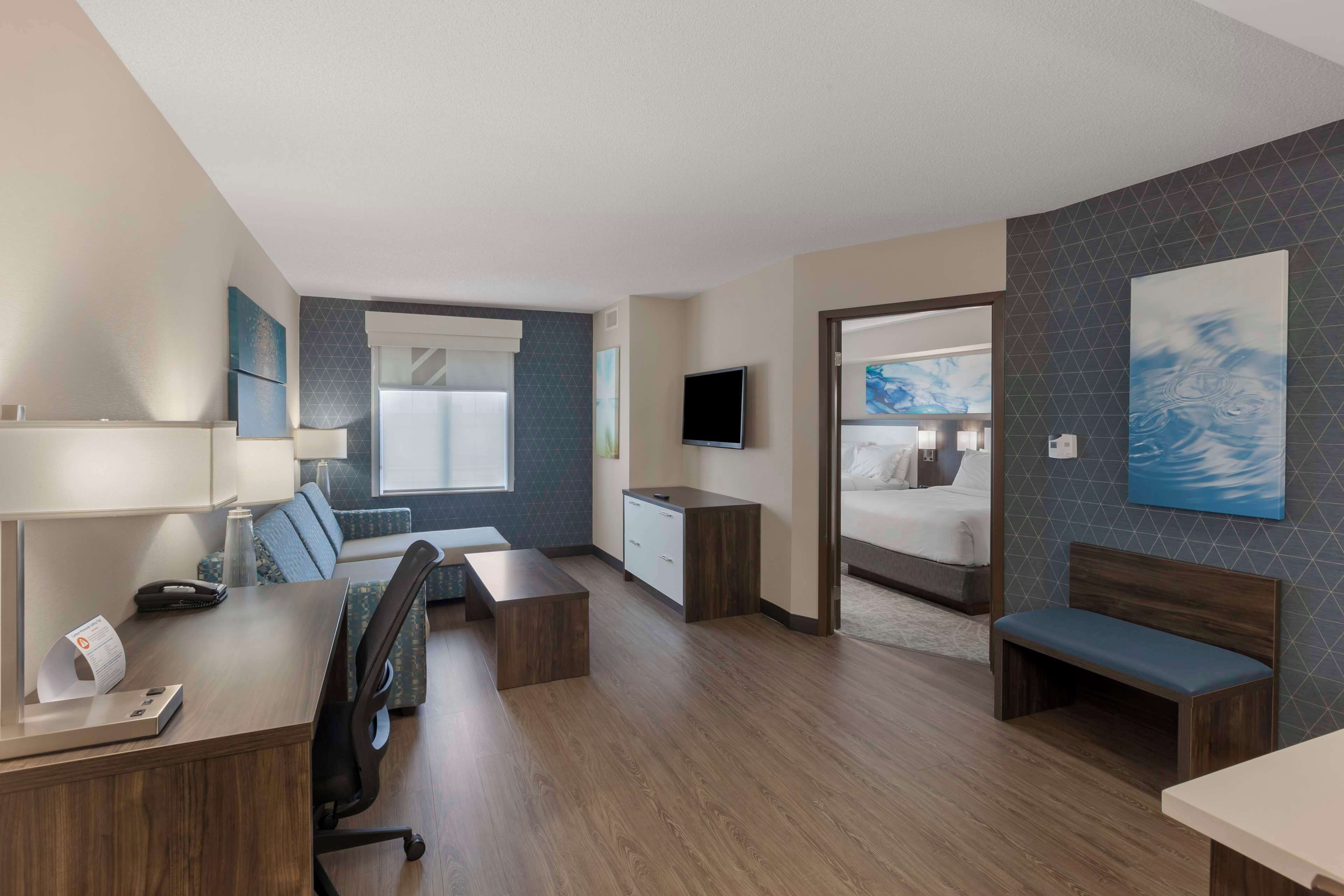 A hotel room with a desk, chair, bed, and artwork on the walls.