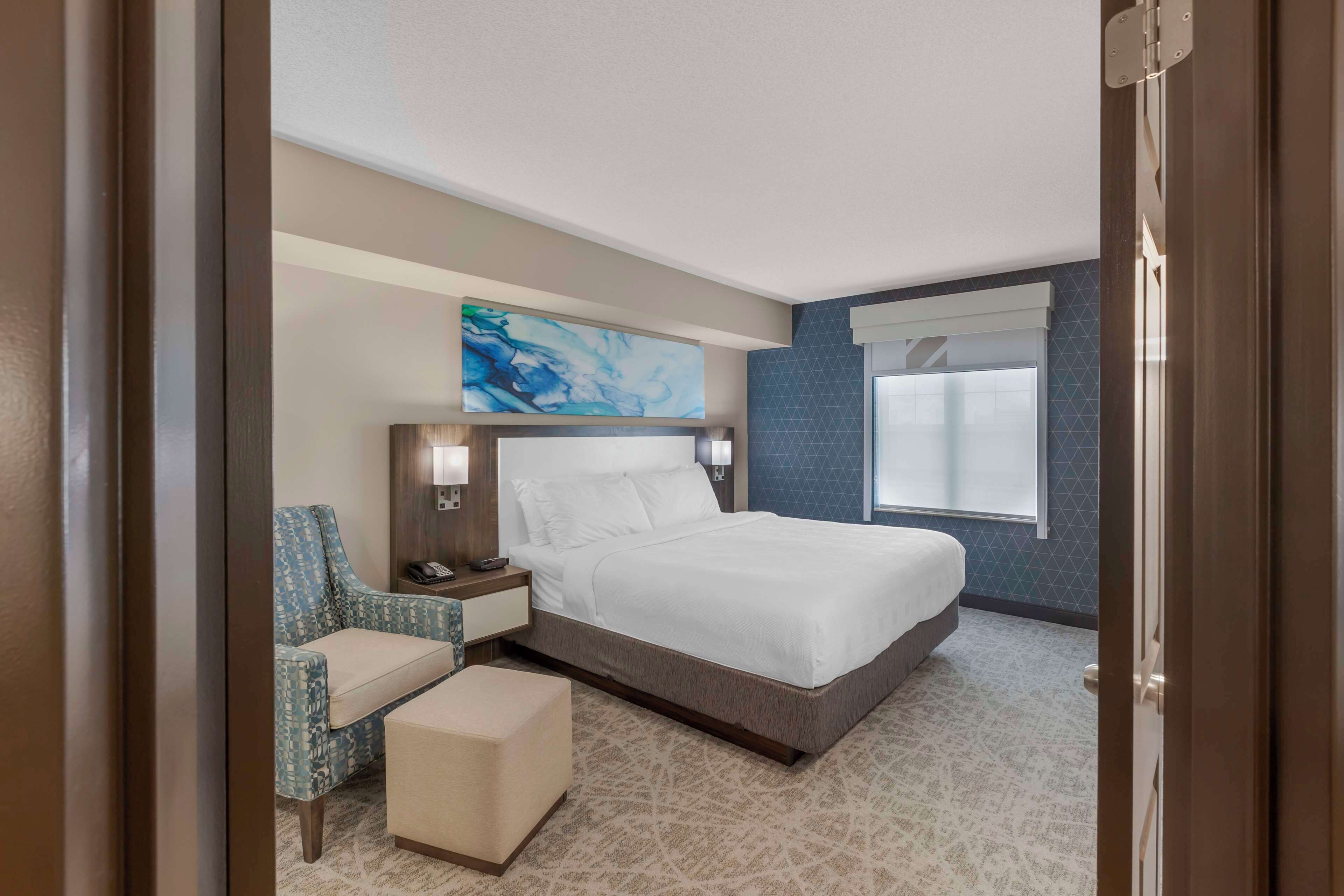Una habitación de hotel con una cama grande, una silla, una mesita y un cuadro en la pared.