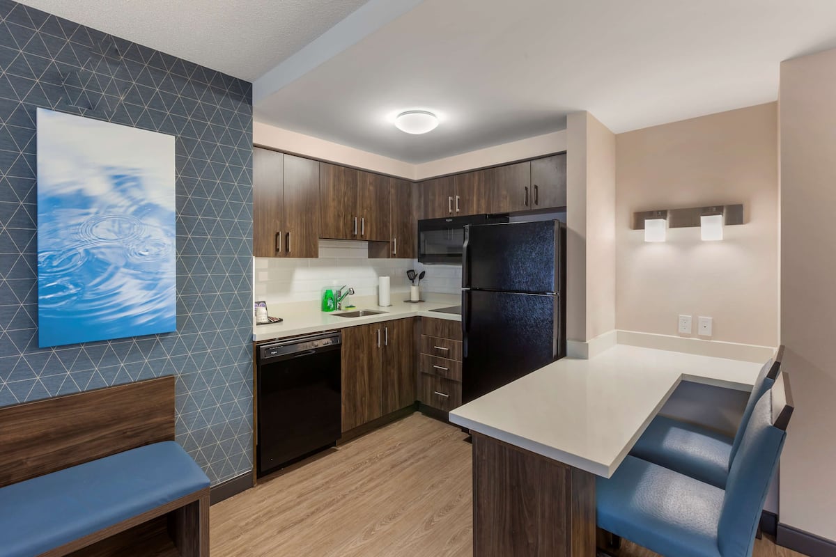 Una cocina moderna con armarios de madera, un refrigerador negro y una encimera blanca.