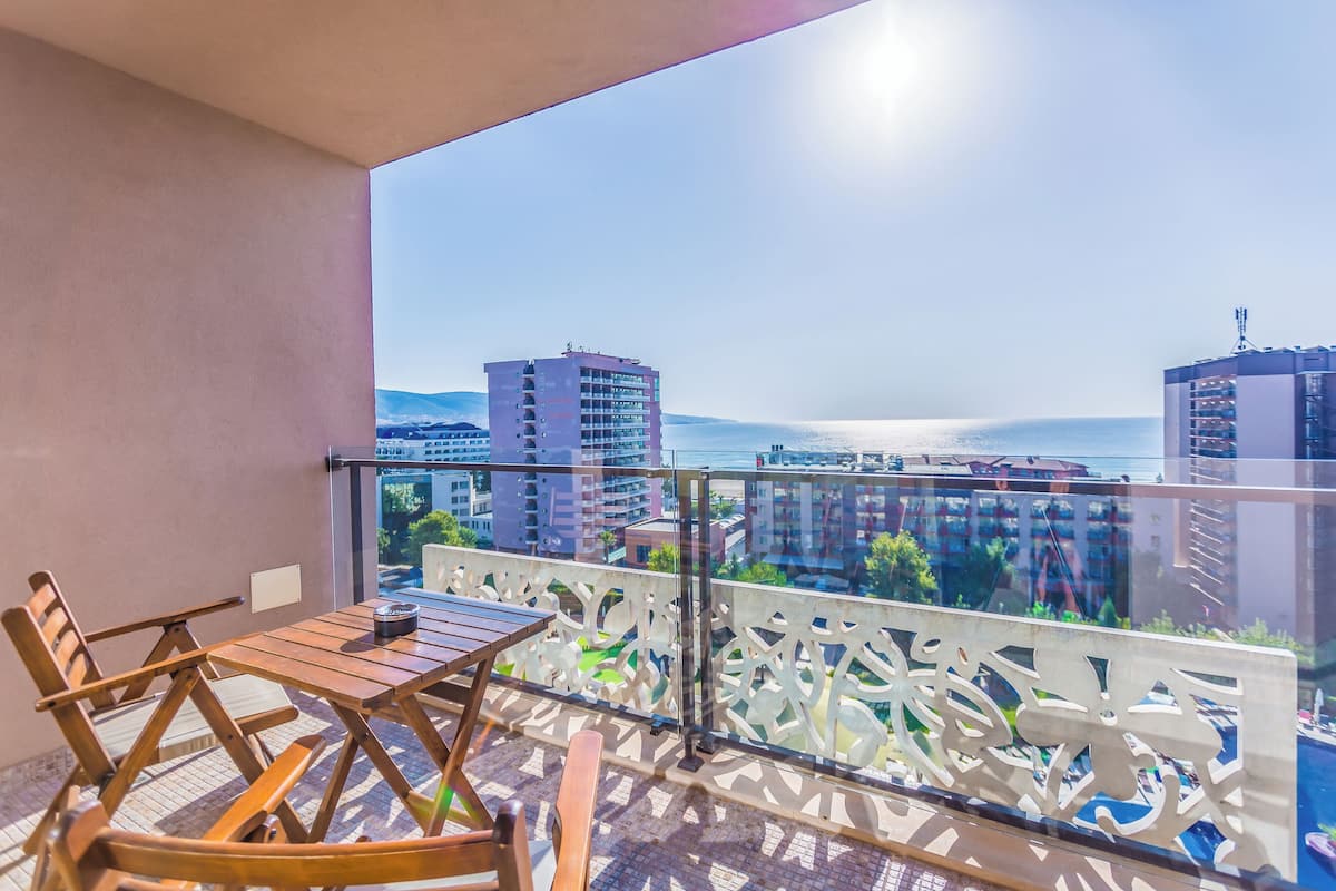 A balcony with a table and chairs, a glass railing, and a view of buildings and water.