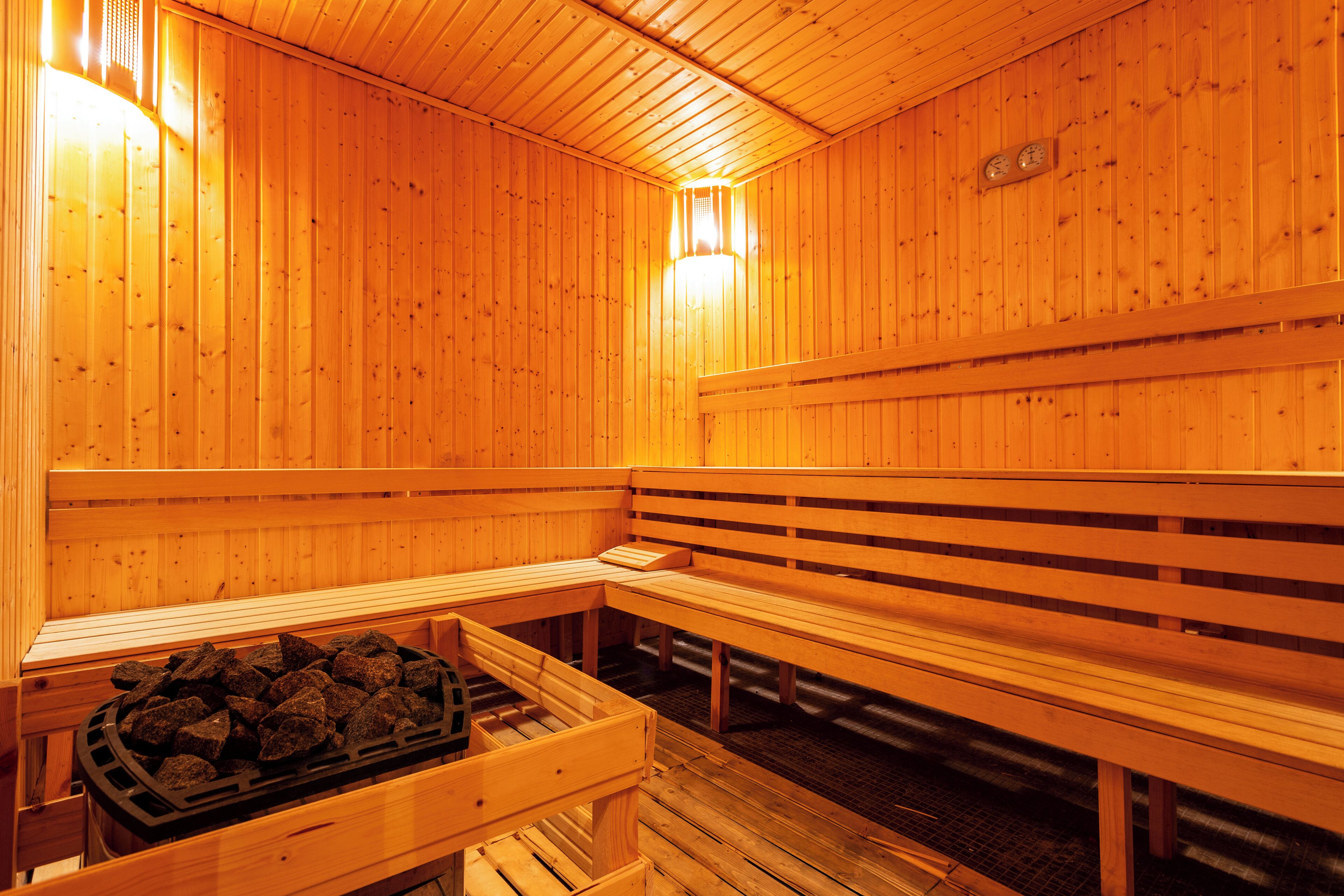 A wooden sauna with benches and a bench with a tray of rocks.