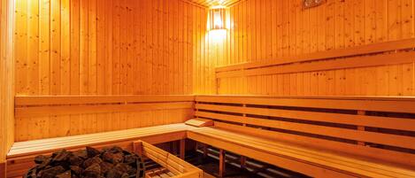 A wooden sauna with benches and a bench with a tray of rocks.