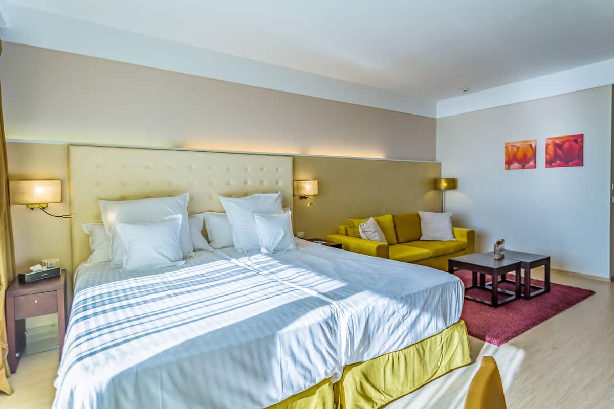 A hotel room with a large bed, a yellow sofa, a small table, and two wall-mounted lamps.