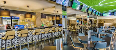 A modern bar area with multiple screens, a Pepsi refrigerator, and a variety of seating options.