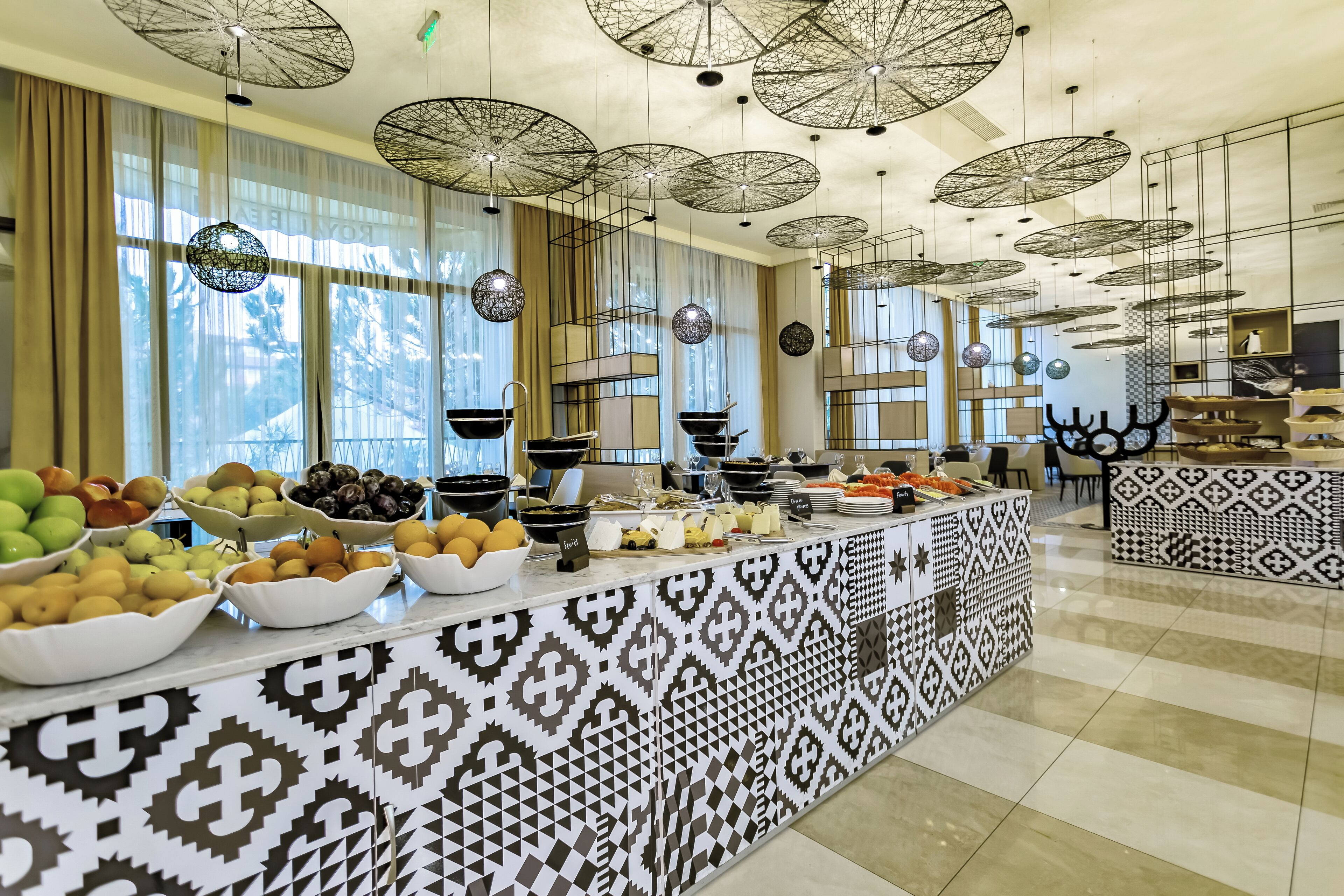 A buffet with various fruits and dishes, patterned tiles, and hanging umbrellas.