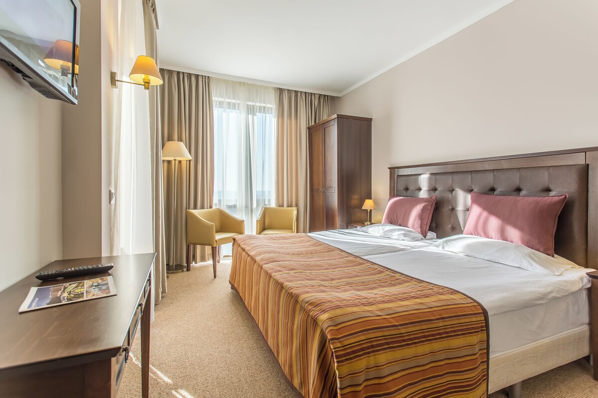 Ein Hotelzimmer mit Bett, Schreibtisch, Fernseher, Stuhl und Kleiderschrank.