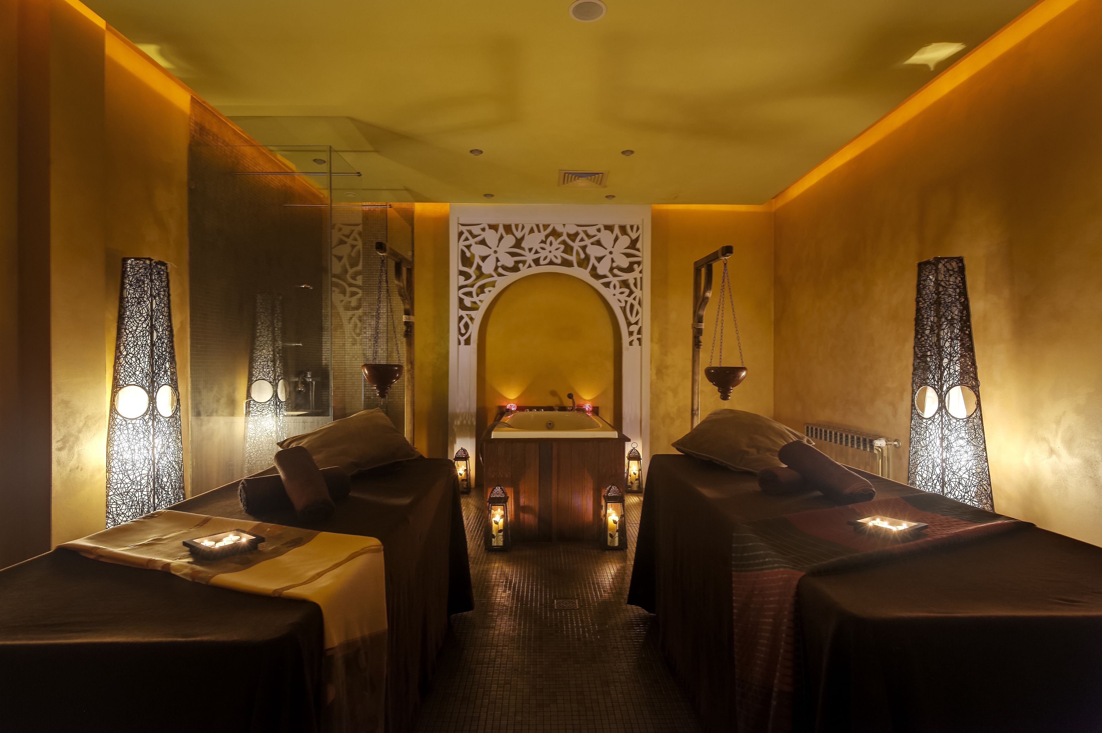 A spa room with two massage tables, a central sink, and decorative wall panels.