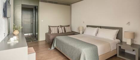 A modern hotel room with a large bed, bedside tables, a desk with a chair, and a small plant.
