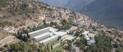 An aerial view of a hillside town with buildings, roads, and a swimming pool.