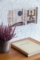 A book titled "DELPI" on a wooden table, a potted plant with purple flowers, and a textured wall with a framed picture.