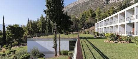 Un edificio moderno con tetto piatto, circondato da prato e siepi curati, con montagne sullo sfondo.