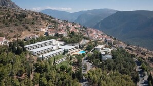 A hillside village with traditional buildings, a modern building with a swimming pool, and mountainous terrain in the background. - Amalia Hotel Delphi (Delphi)
