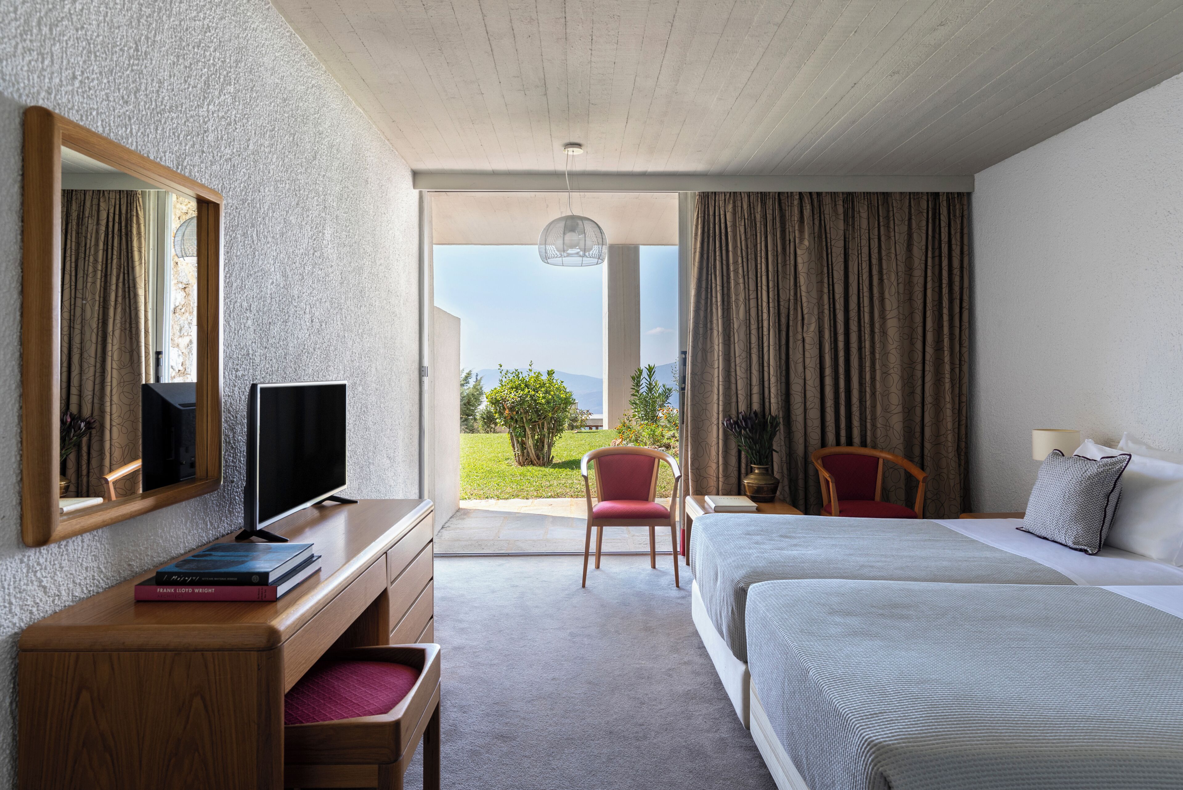 Habitación de hotel con cama, escritorio con televisor, silla, espejo grande y vistas al exterior.