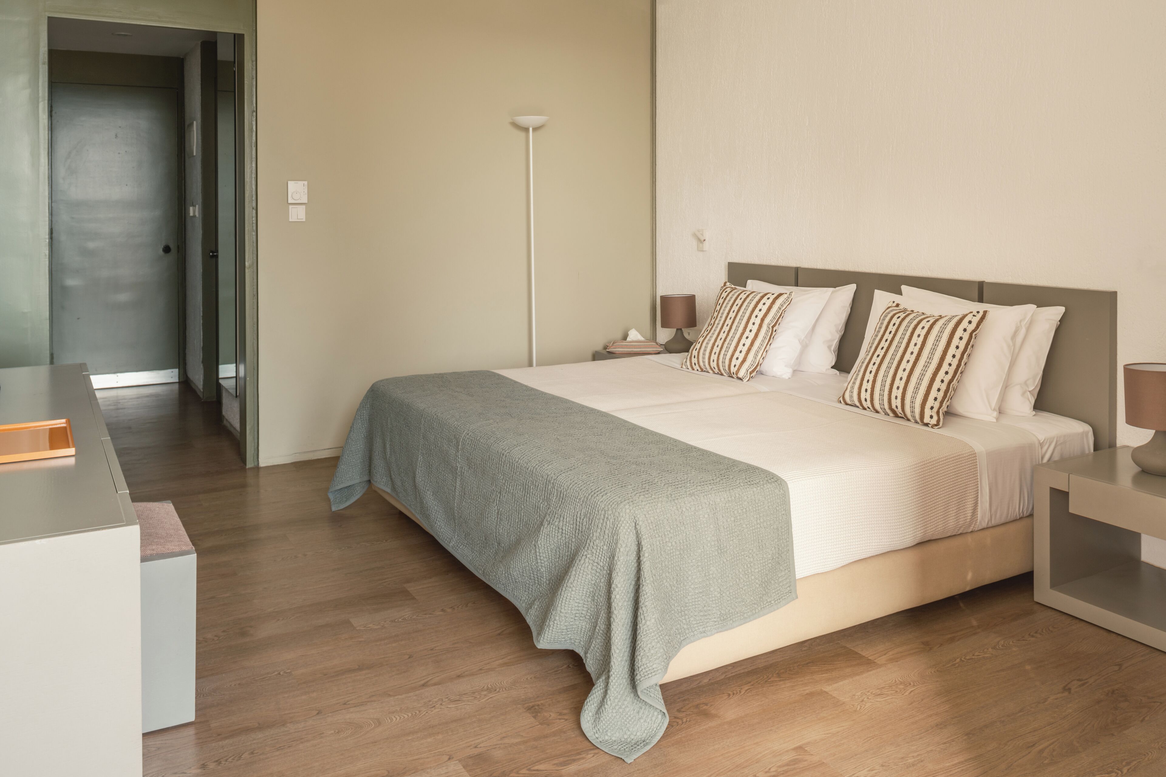 A modern bedroom with a large bed, bedside tables, a floor lamp, and a desk.