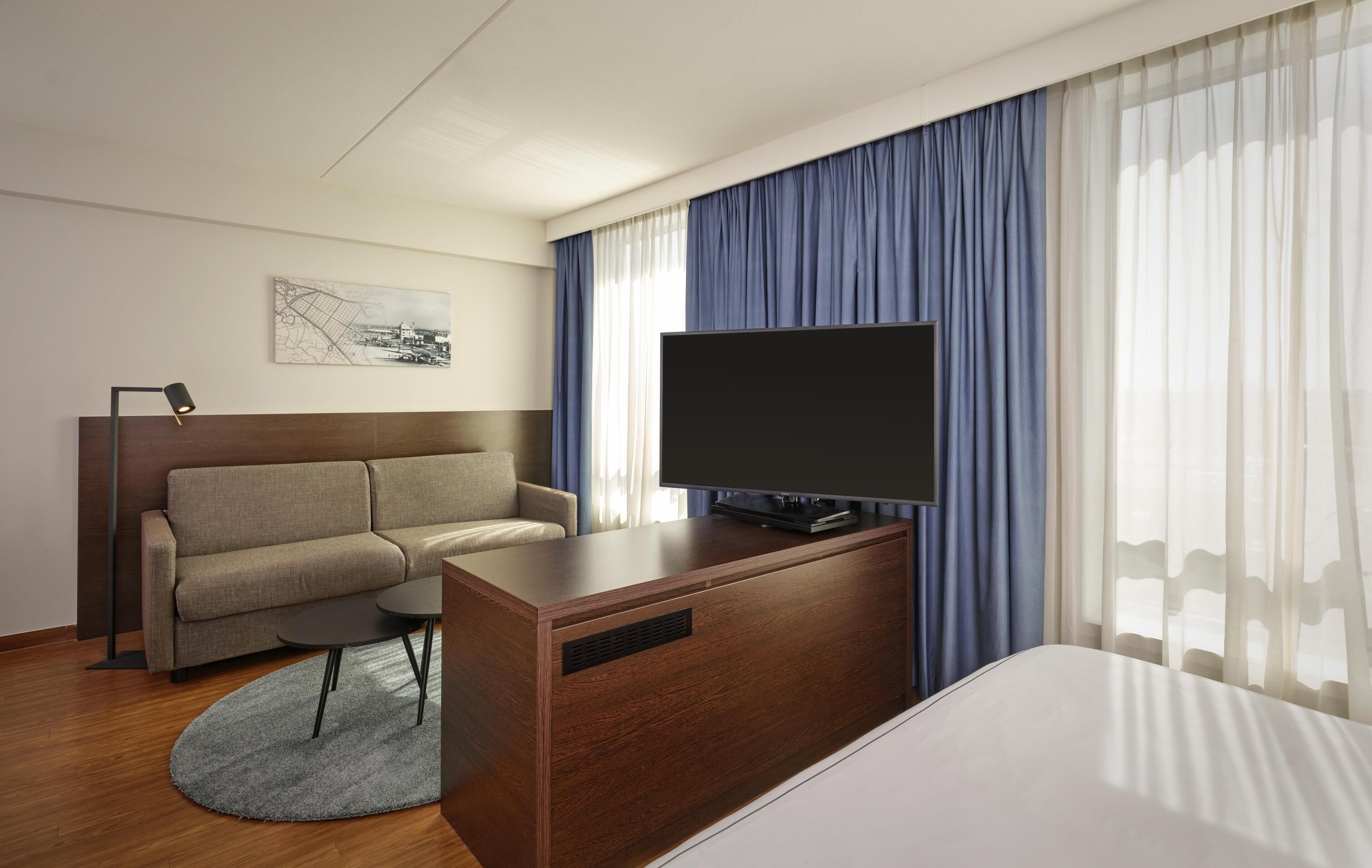 Une chambre d’hôtel comprenant un lit, un canapé, un bureau avec un téléviseur à écran plat, une petite table et un tapis.