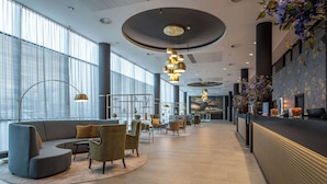 A modern lobby with a curved sofa, armchairs, and a reception desk. - Park Plaza Amsterdam Airport (Lijnden)