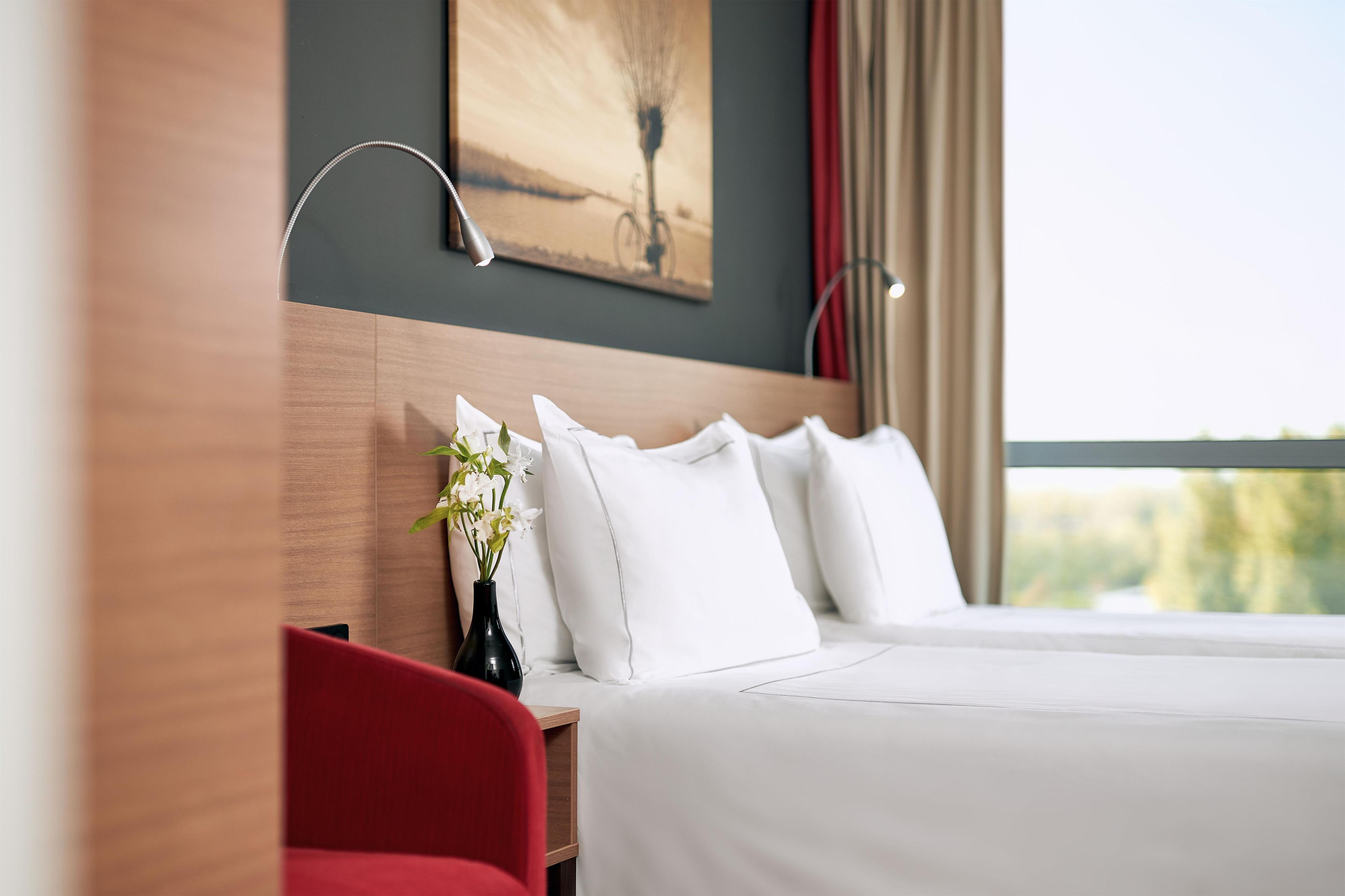 A hotel room with a large bed, a bedside table with a vase of flowers, and a painting on the wall.