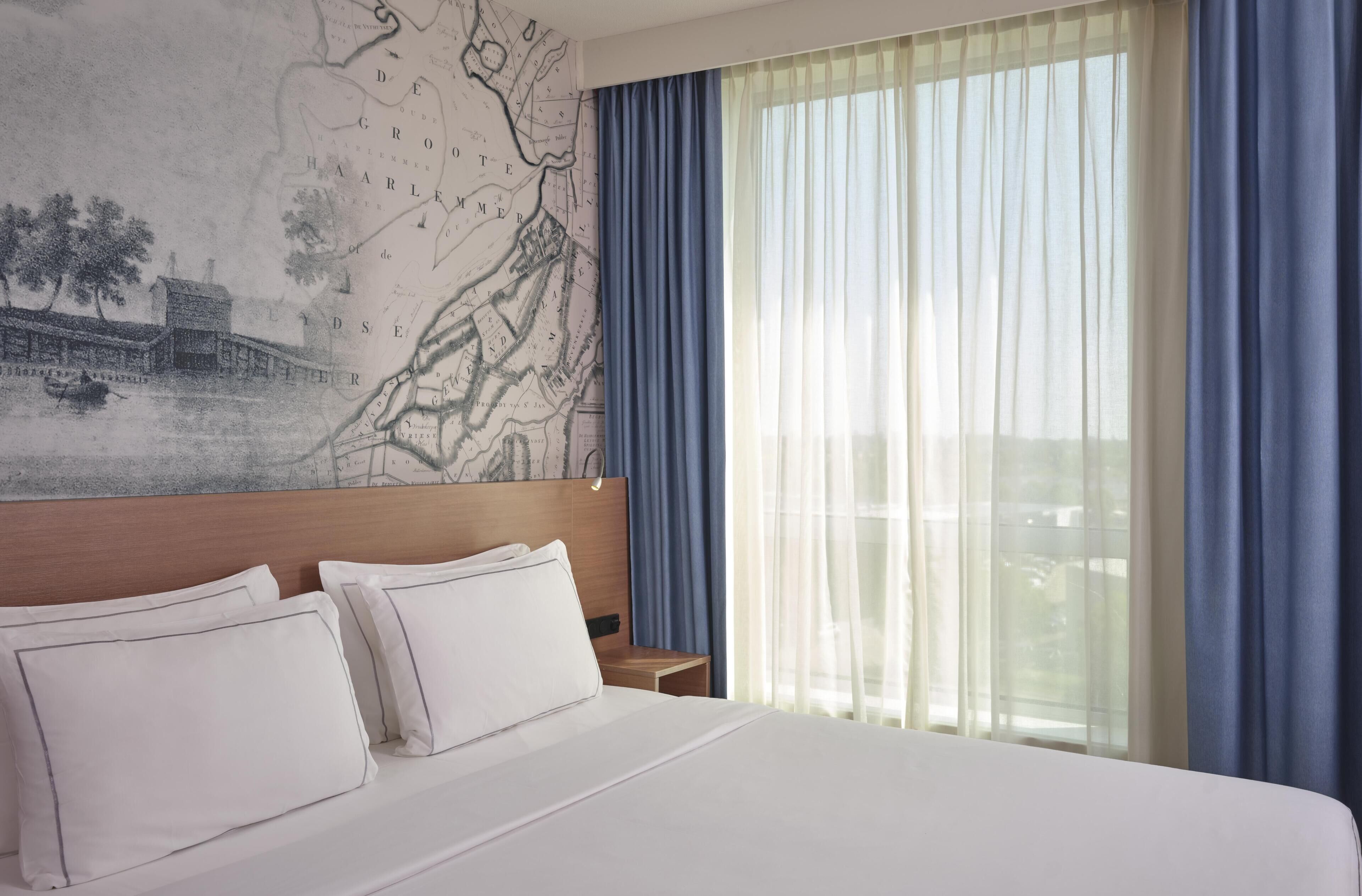 Een hotelkamer met een groot bed, een hoofdeinde, een nachtkastje en een wereldkaart aan de muur.