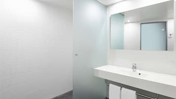 A modern bathroom with a white tiled wall, a glass shower enclosure, and a white sink with a mirror above it.