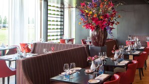 A restaurant with a large ceiling projection, red upholstered booths, and a central floral arrangement. - Park Plaza Amsterdam Airport (Lijnden)