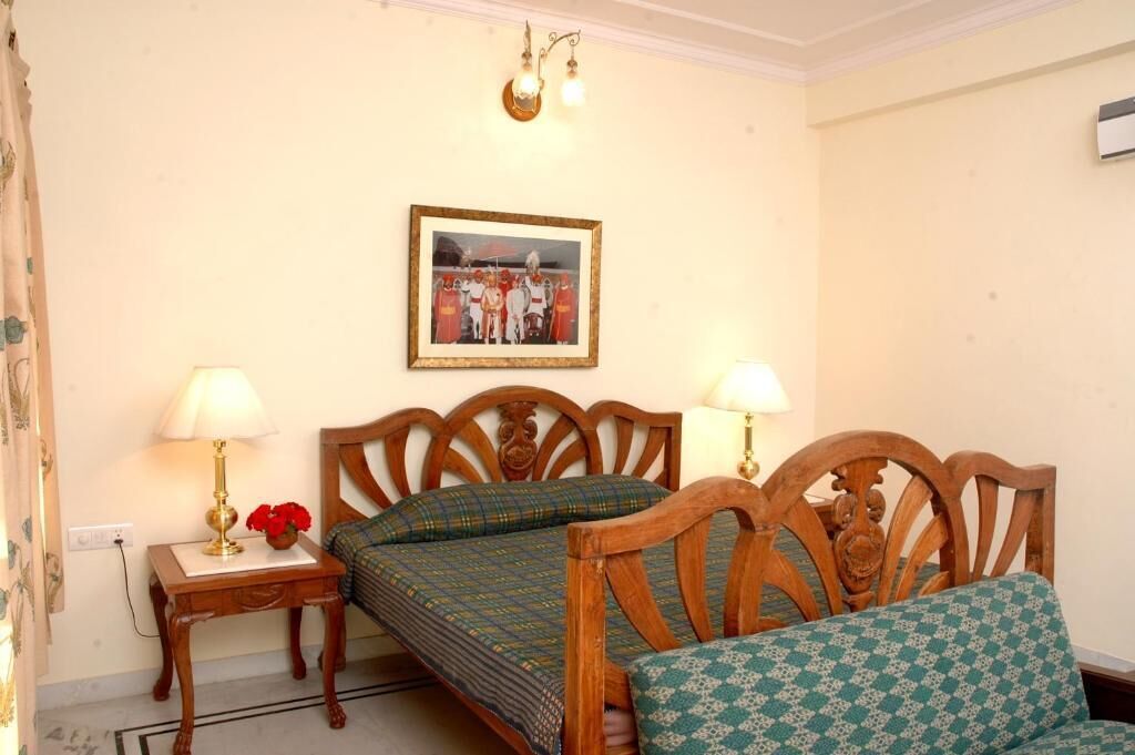A bedroom with two wooden beds, a bedside table with a lamp, a framed picture on the wall, and a window with curtains.