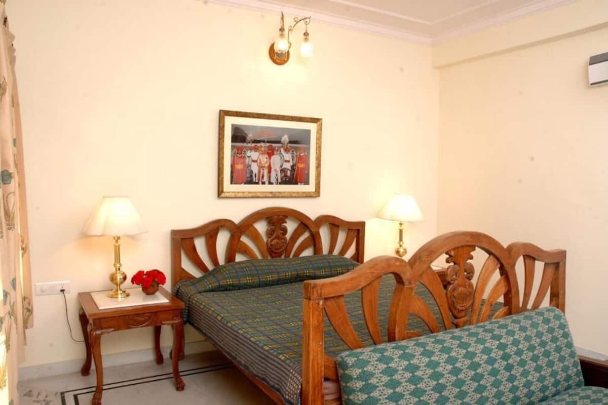 A bedroom with two wooden beds, a bedside table with a lamp, a framed picture on the wall, and a window with curtains.