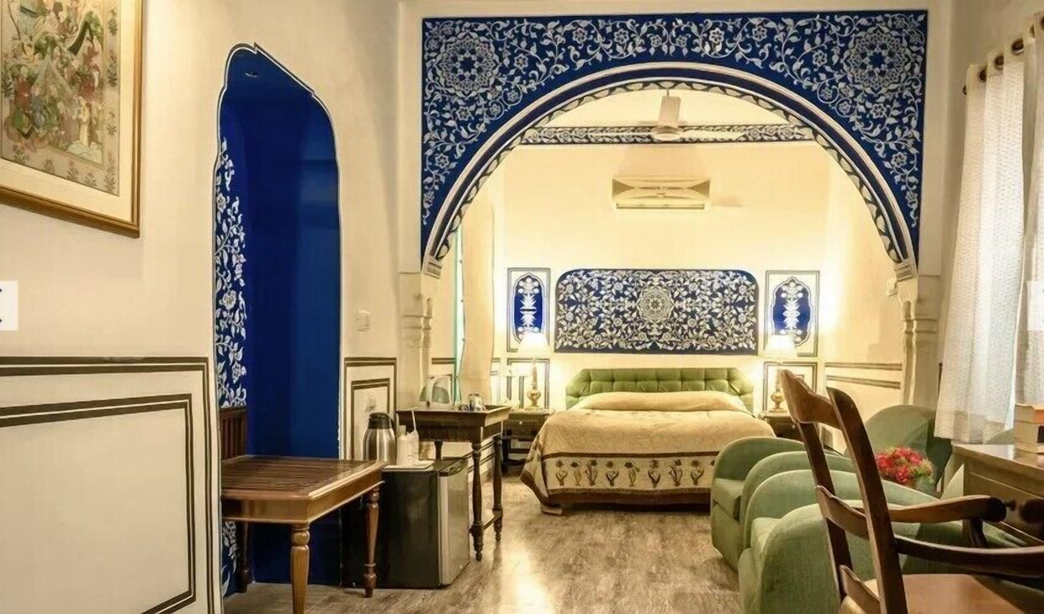 A room with a bed, a desk, a chair, and a decorative archway.