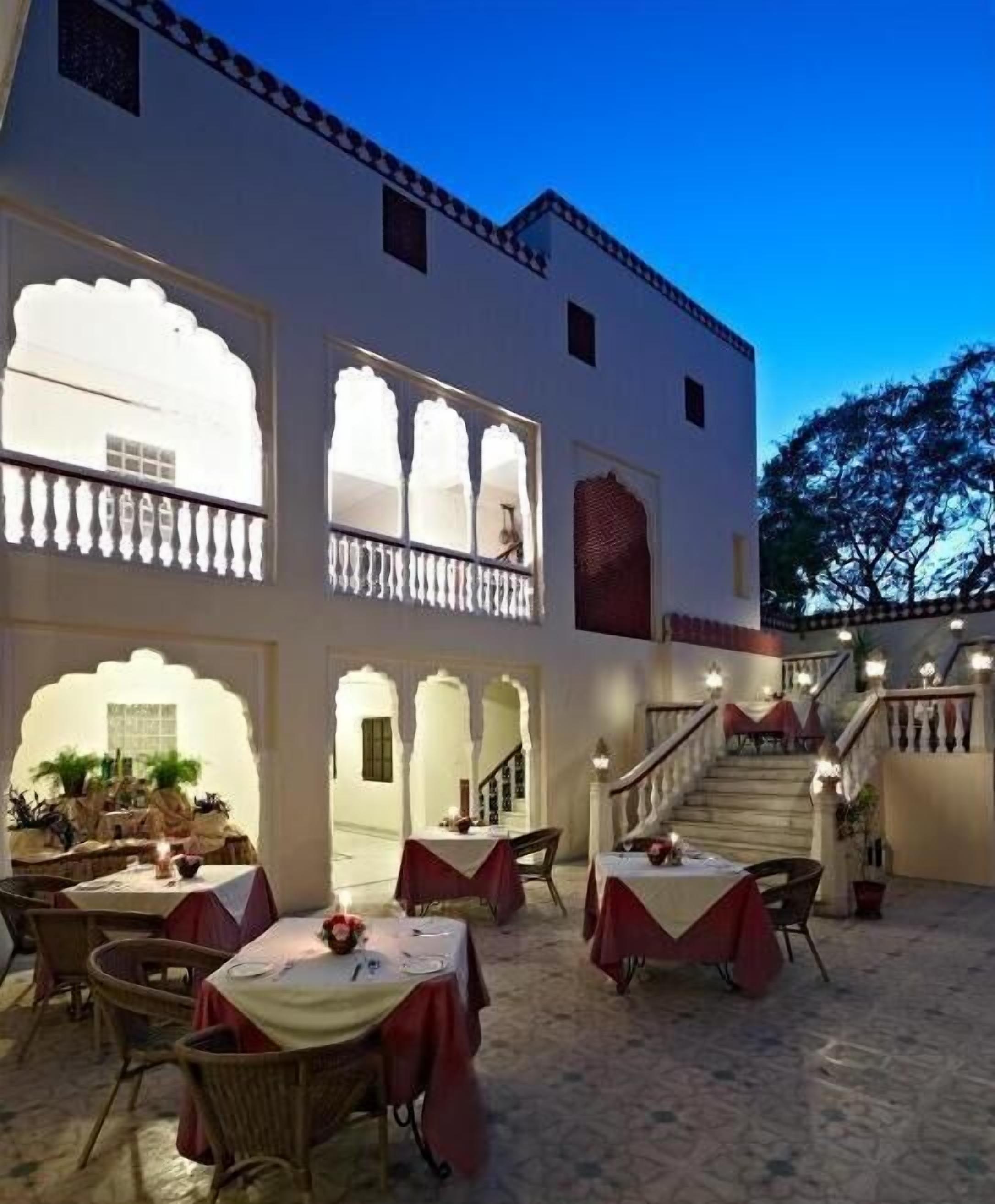 A traditional building with multiple dining areas, each with tables and chairs, set against a clear sky.