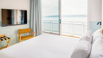 Habitación de hotel con cama, una silla, televisor y balcón con vista al agua.