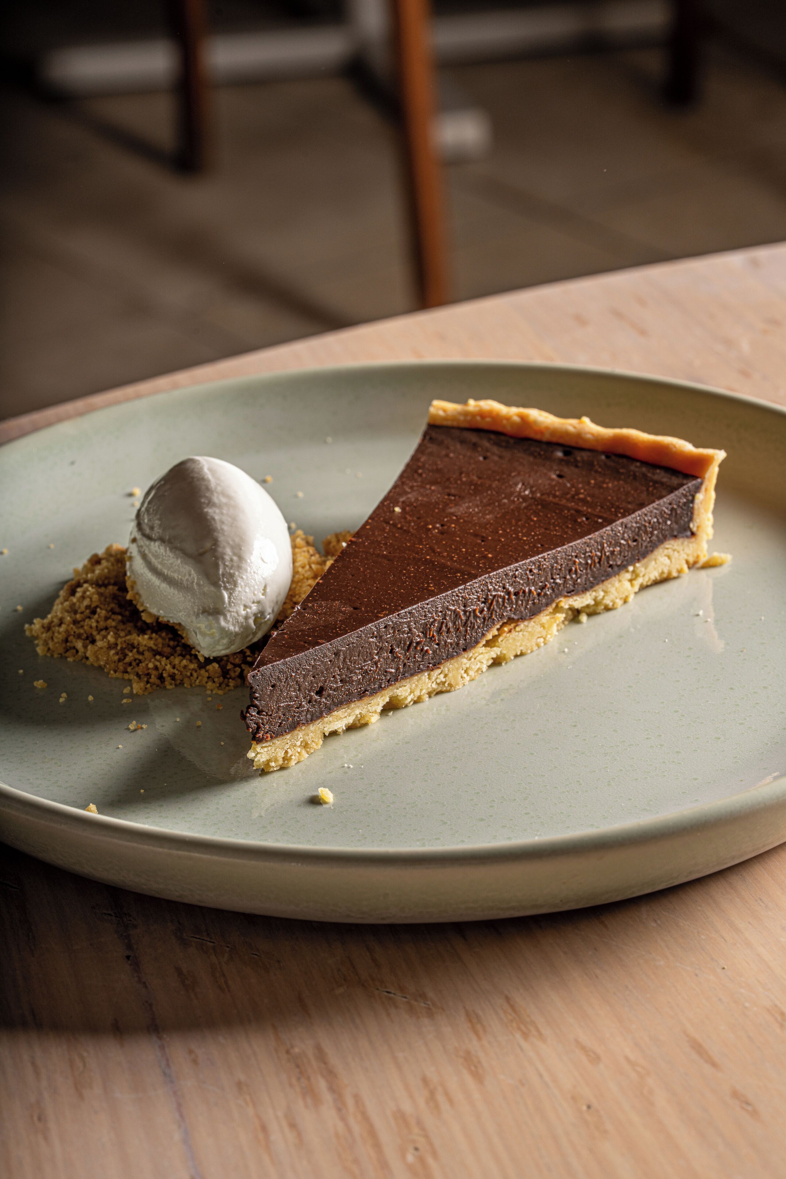 A slice of chocolate tart with a scoop of ice cream on a ceramic plate.