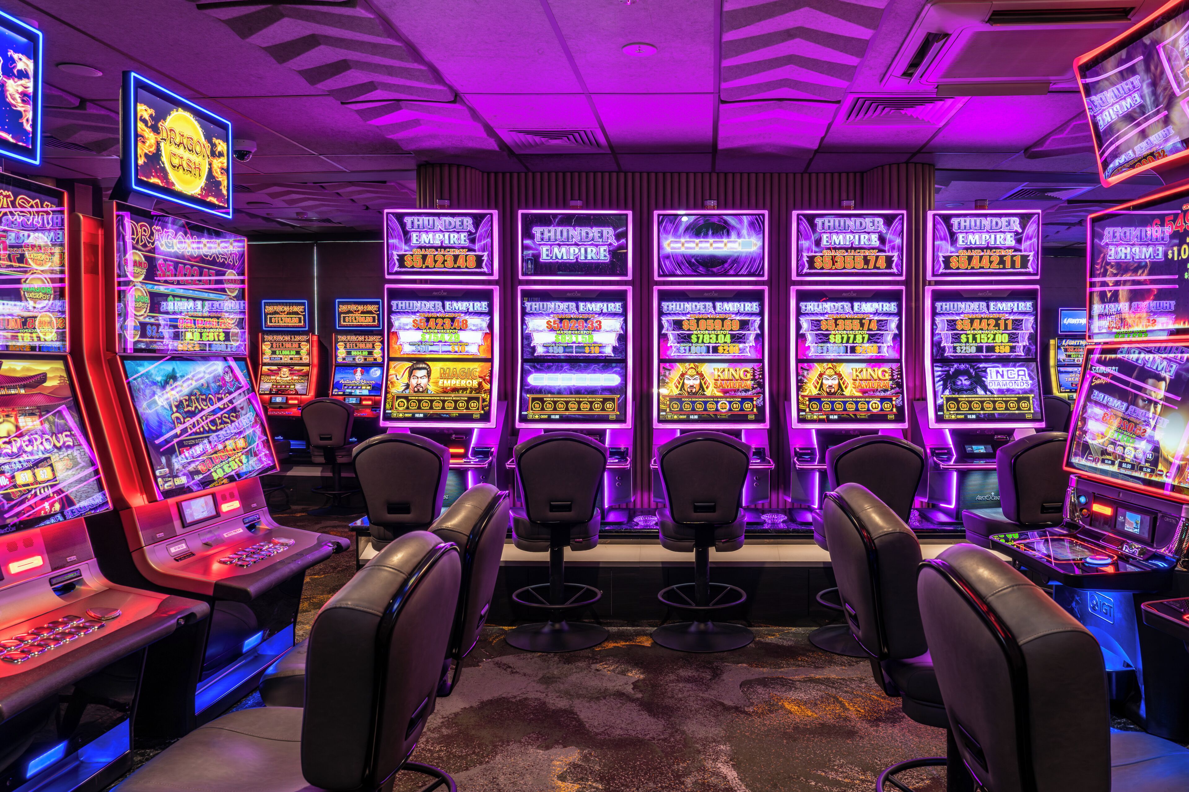 Een casino met gokkasten, speeltafels, stoelen voor spelers en neonverlichting.