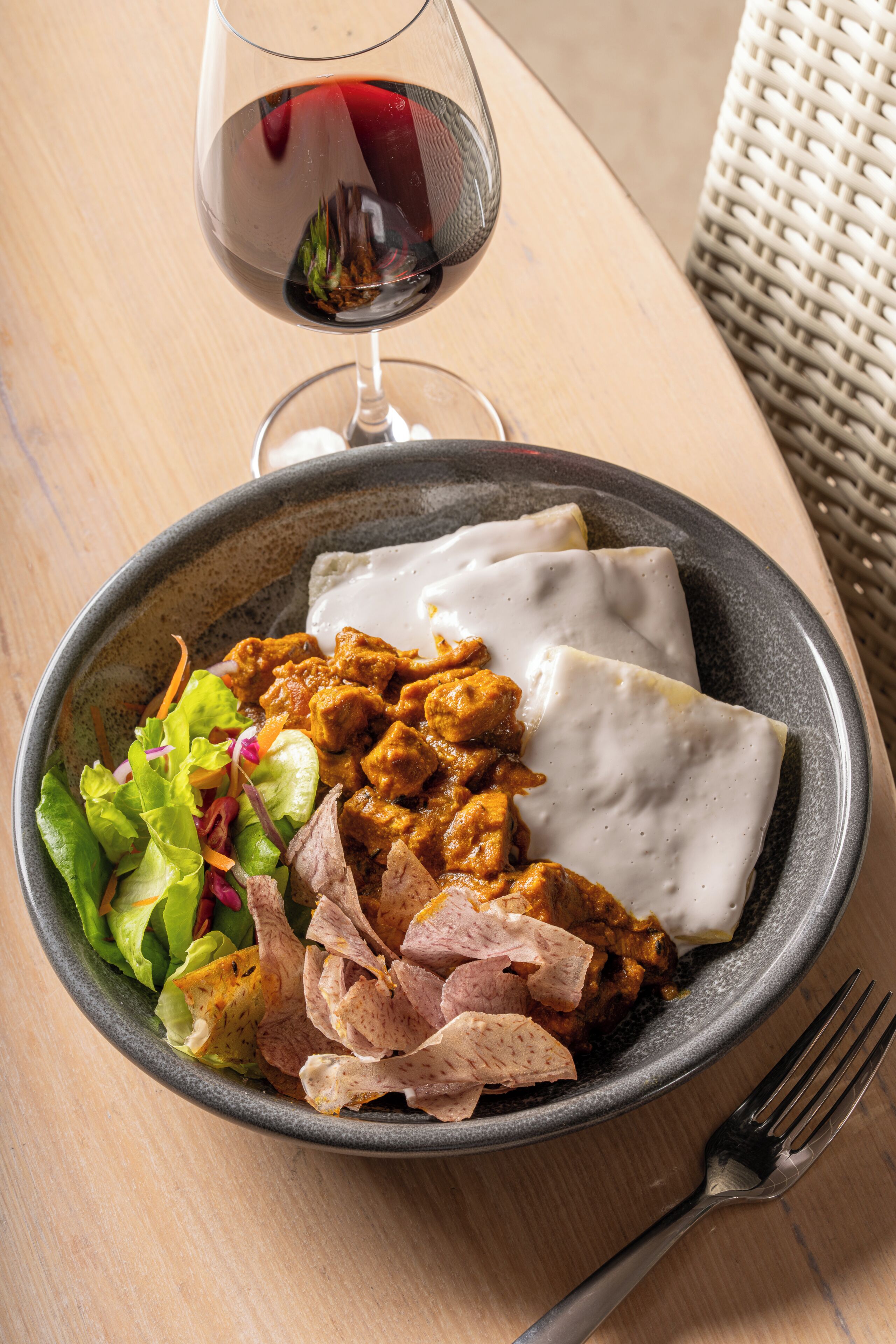 A bowl of food with a glass of red wine on a wooden table.