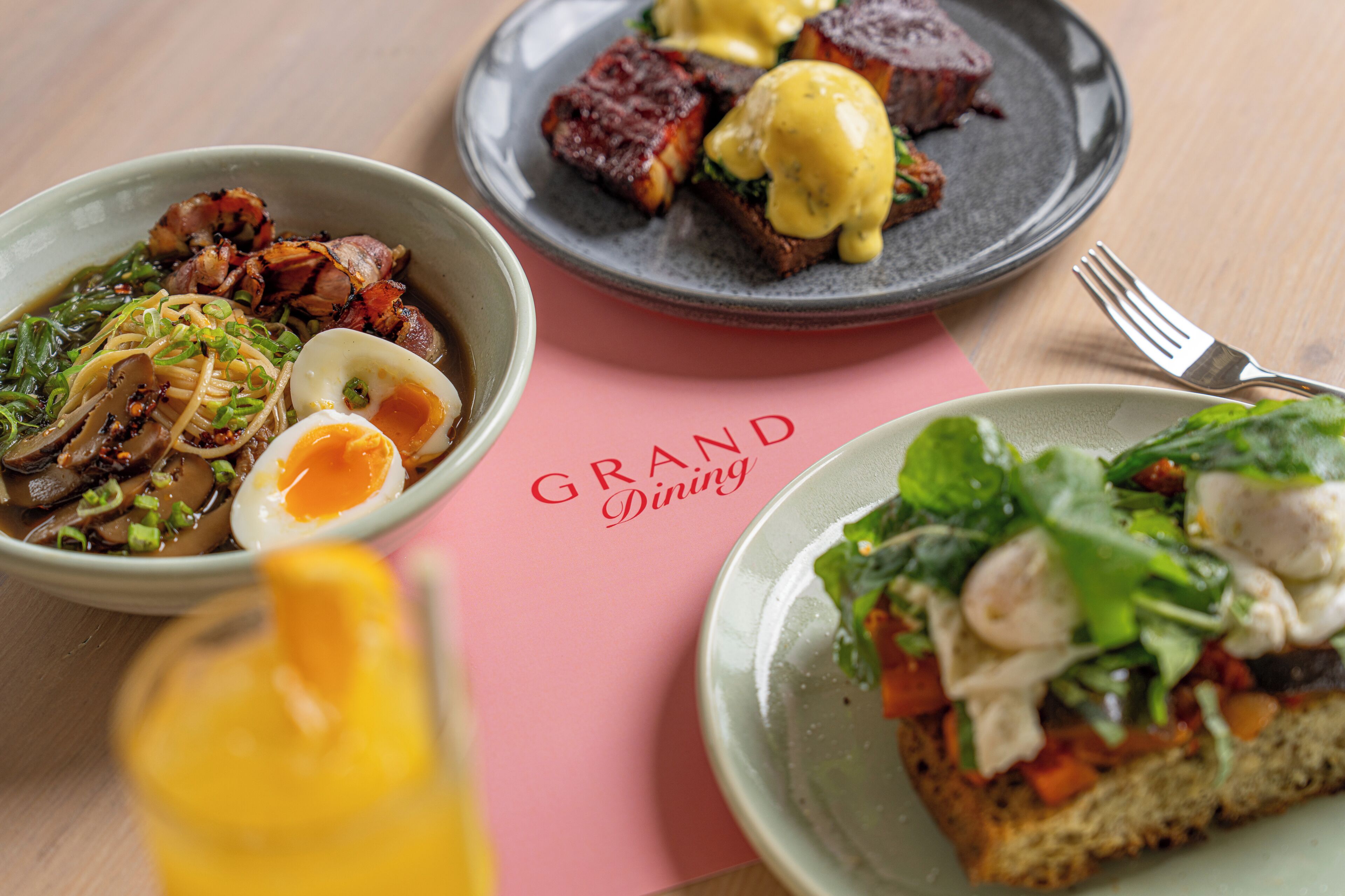 A table with three plates of food, a fork, and a menu titled 'GRAND Dining'.