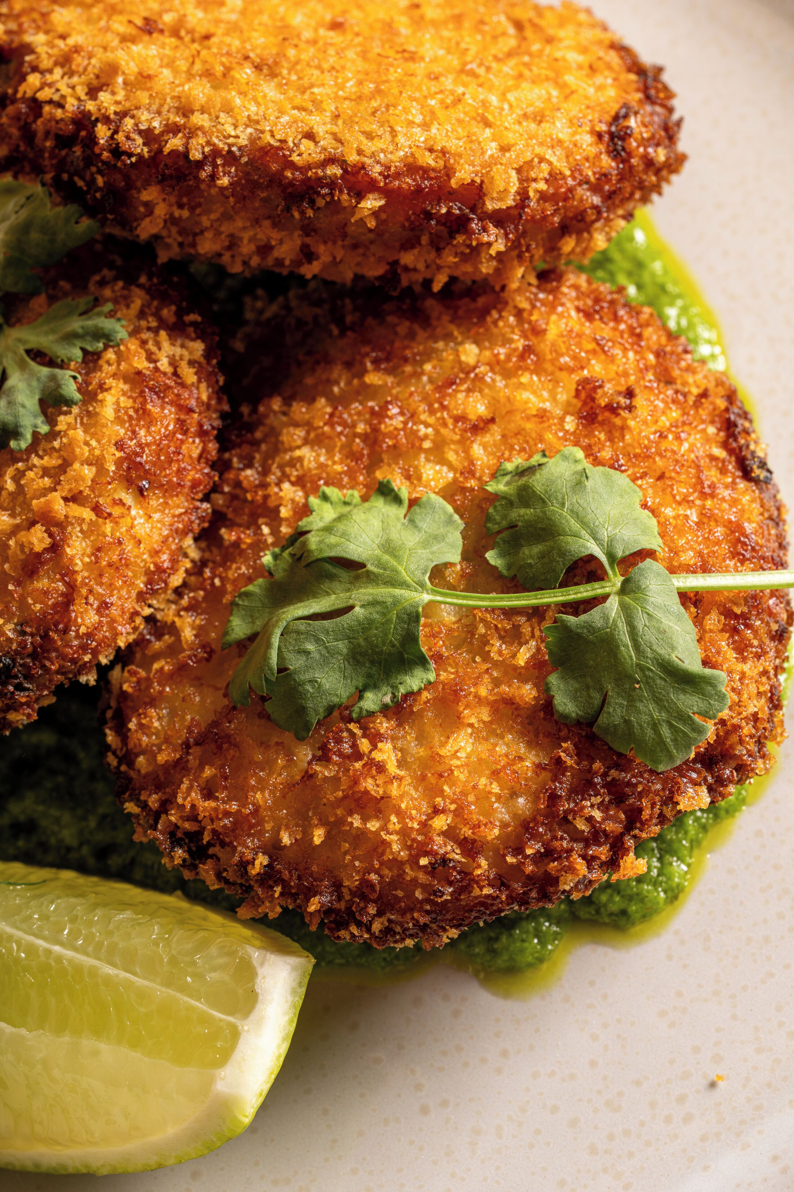 Un plato de comida empanizada y frita, adornado con un gajo de lima y cilantro.