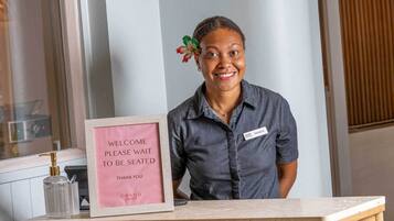 Mostrador de recepción con un cartel que dice 'WELCOME PLEASE WAIT TO BE SEATED THANK YOU GRAND Dining'.