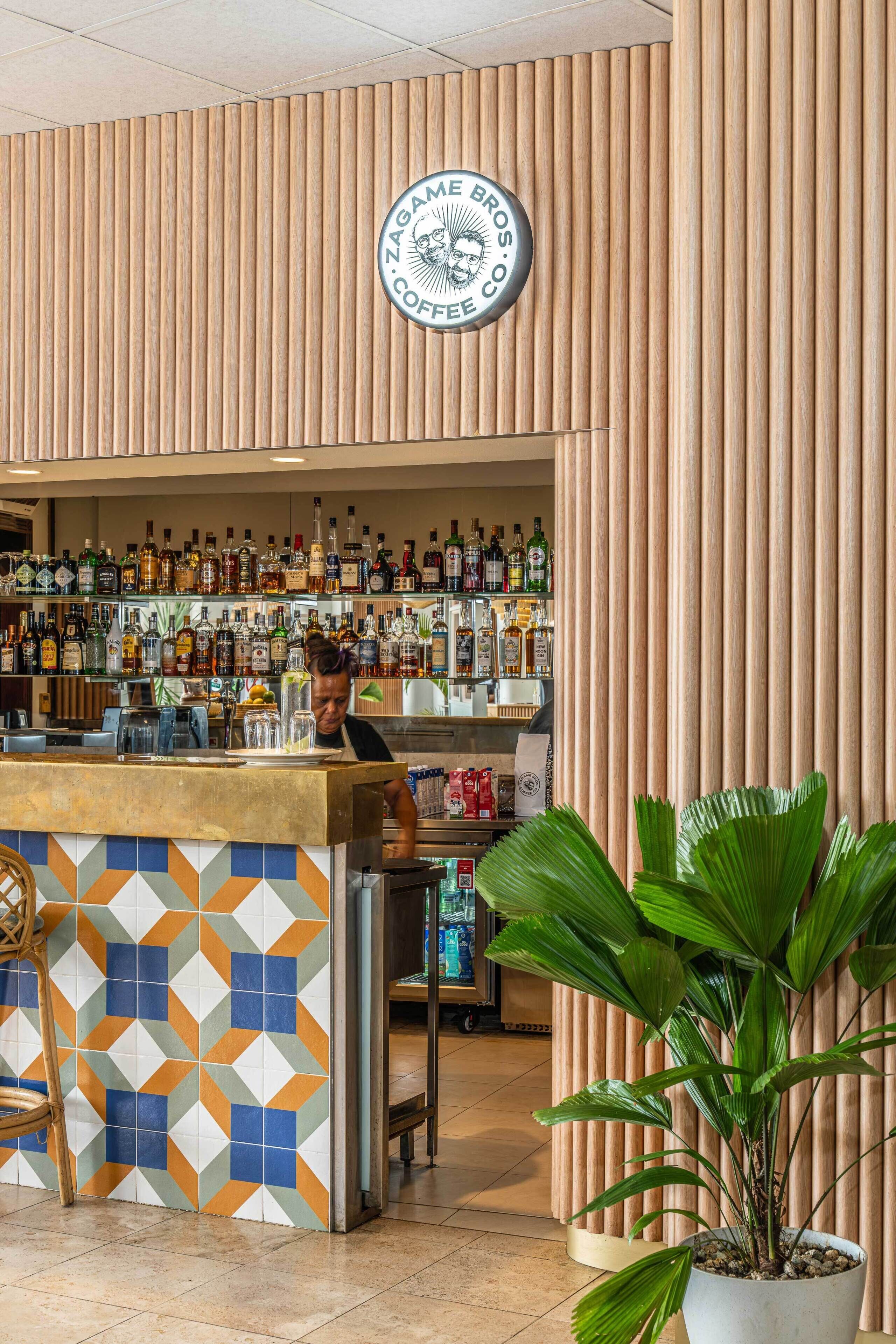 A bar area with a wooden slat wall, a circular logo above the bar, and a variety of liquor bottles on shelves.