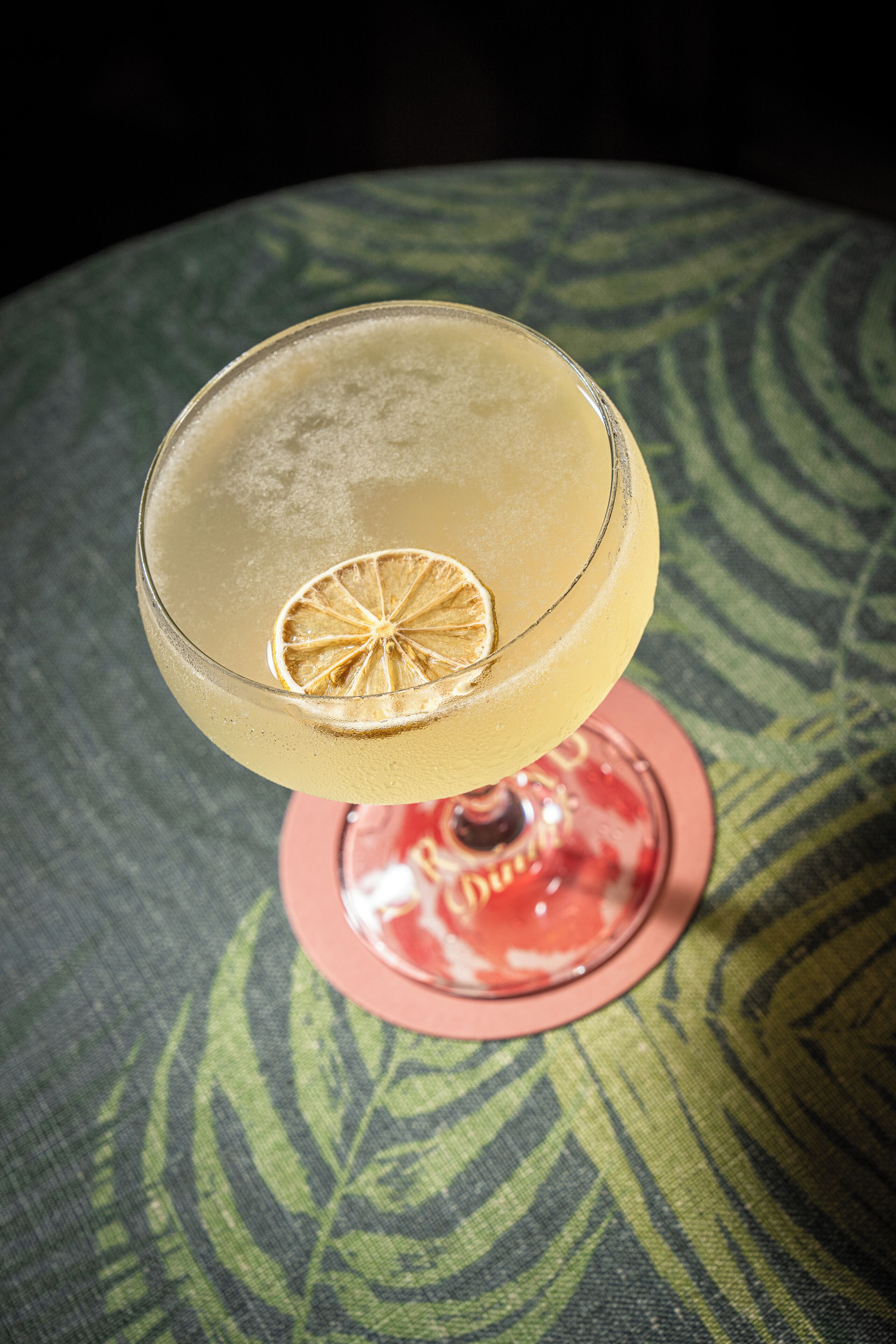 A cocktail glass with a slice of citrus on a patterned tablecloth.