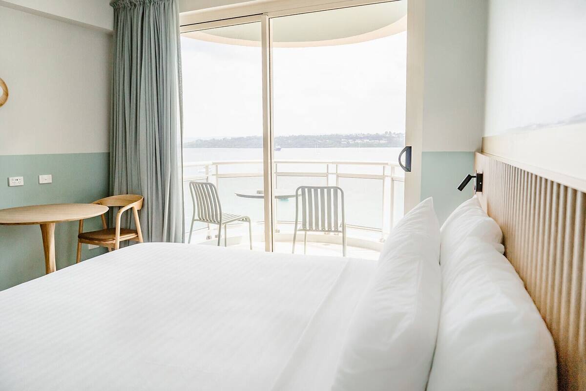 A hotel room with a bed, a small table, two chairs, and a balcony with a view of the sea.