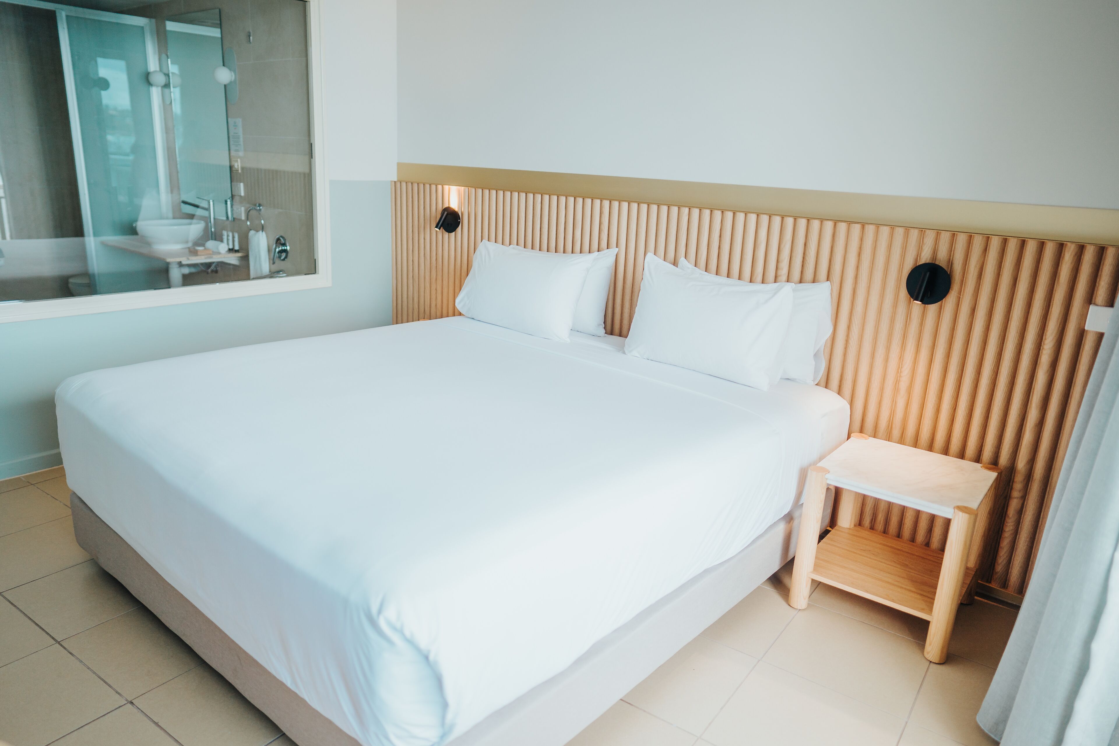 A large bed with white linens, a wooden headboard, and a small wooden nightstand with a white drawer.
