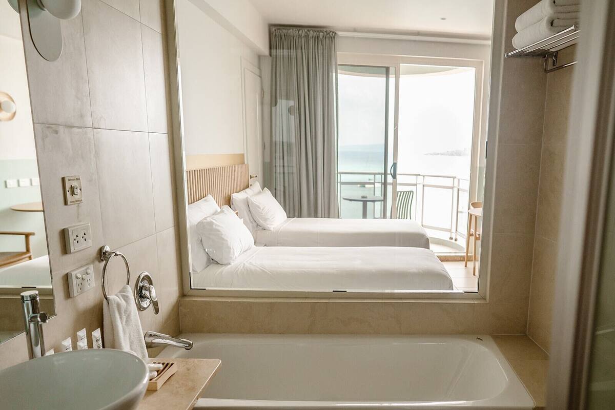 A hotel room with a large bathtub, two beds, a balcony with a view, and a bathroom with a sink and toiletries.